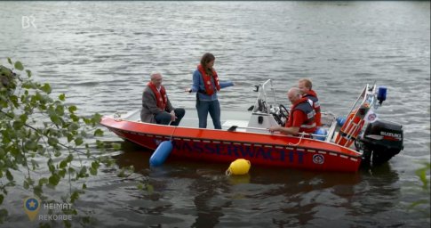 Auf einem Gewässer sind vier Personen in Schwimmwesten auf einem Boot der Wasserwacht.