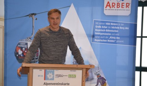 Präsident Wolfgang Bauer steht vor einem aufgestellten Arber-Hintergrund an einem Rednerpult und hält eine Ansprache.