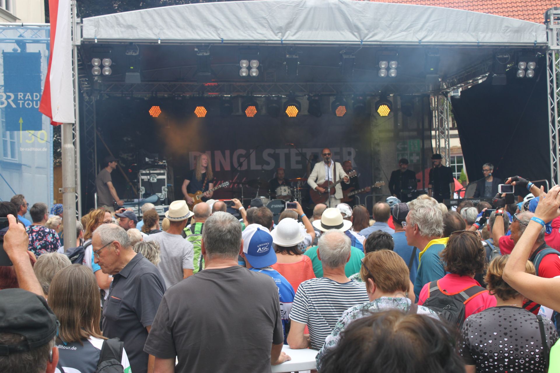Auf einer Bühne performt Hannes Ringlstetter mit einer Band. Davor steht eine Menschenmenge und schaut ihm zu.