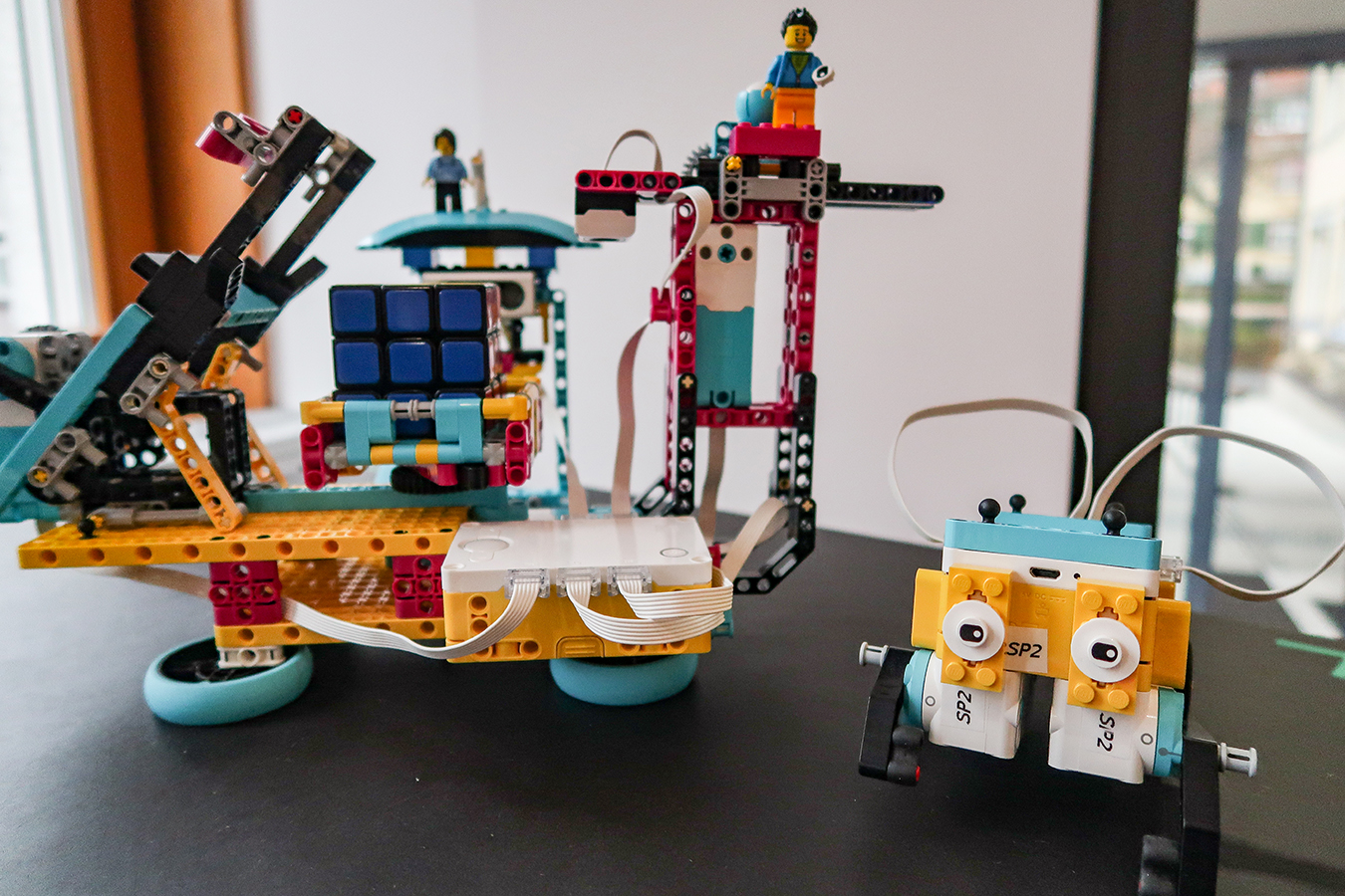 Auf einem Tisch stehen zwei Roboter die aus bunten Legosteinen zusammengesetzt worden sind.