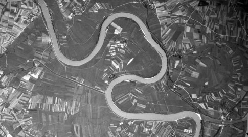 Schwarzweiße Luftbildaufnahme einer Flussschleife umgeben von Feldern.