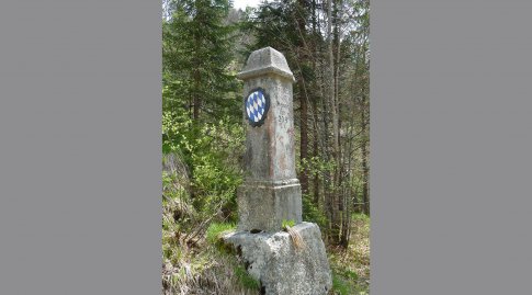 Auf einem Weiserstein in einem Wald ist das Bayerische Wappen zu sehen.