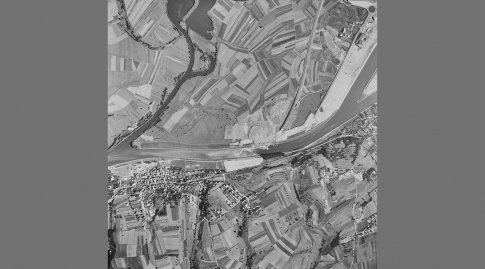 Schwarzweißes Luftbild der Mündung des Main-Donau-Kanals in den Main umgeben von Feldern und einer Häusersiedlung.