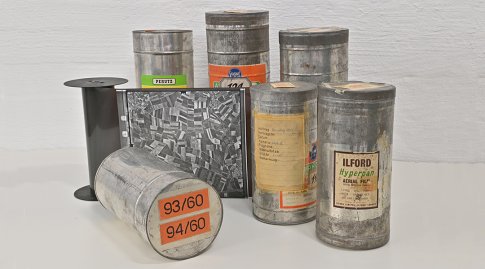 Mehrere Filmdosen für analoge Luftbilder und eine Filmrolle mit einem abgewickelten schwarz-weiß-Luftbild.